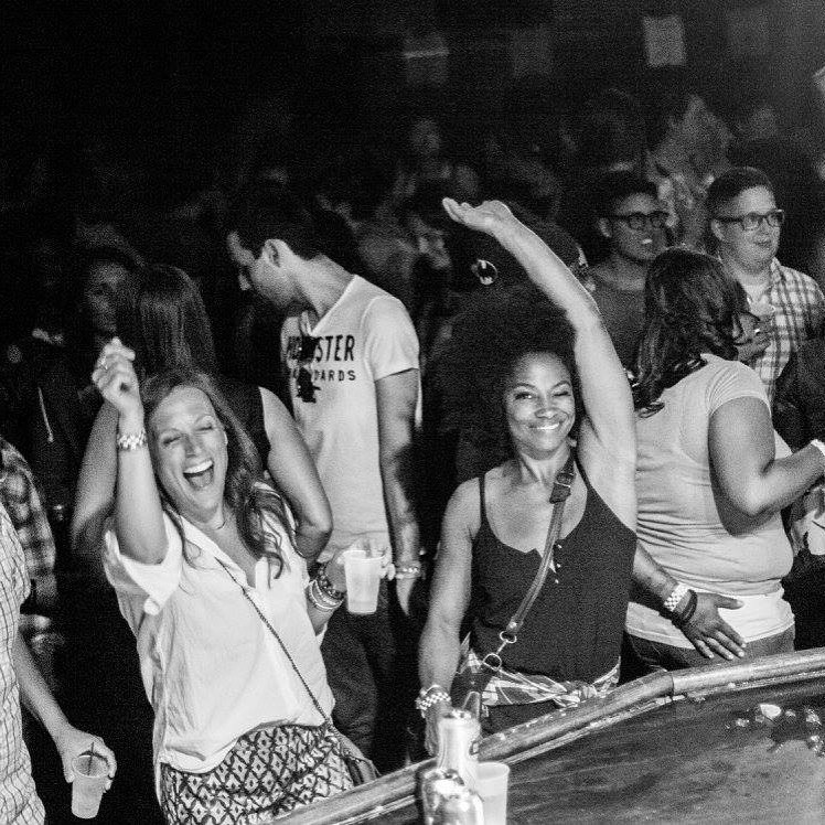 Dancing in the middle of the floor, arm up, mid-laugh, black and white.